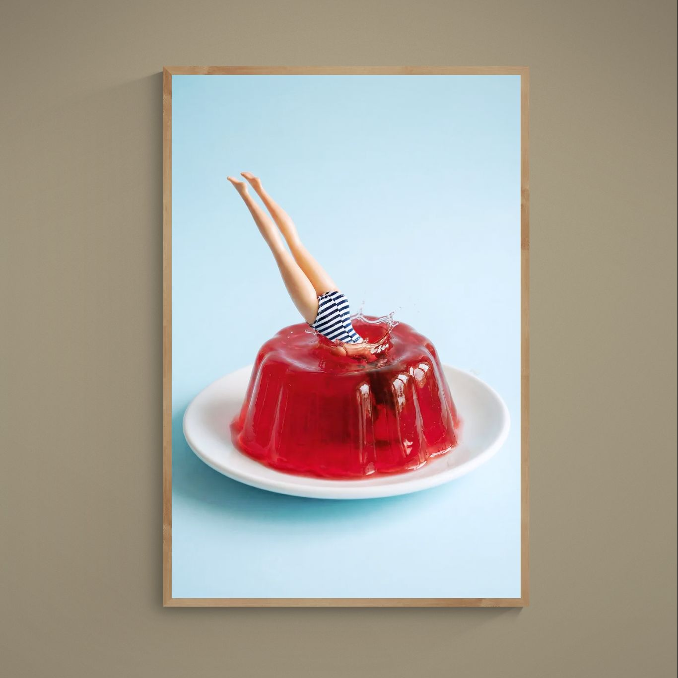 Striped swimsuit legs diving into red gelatin on a plate against a pale blue background